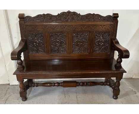 An oak hall bench with foliate carving to back on turned legs and cross streacher