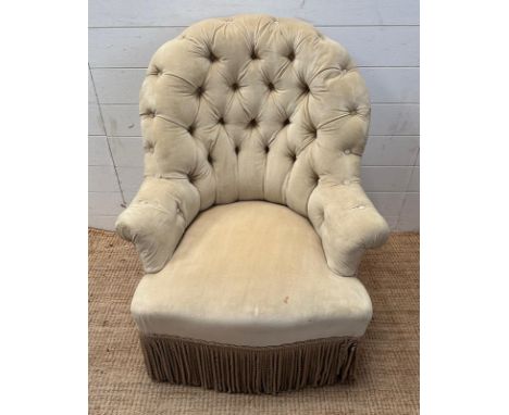 A button backed bedroom armchair upholstered in a light beige fabric 
