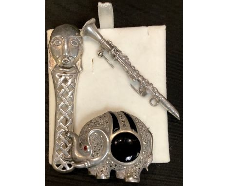 An Arts and Crafts mask brooch; a silver and marcasite Elephant brooch; a silver clarinet 