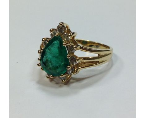 An emerald and diamond ring, the pear shaped emerald surrounded by small round brilliant cut diamonds, all claw set to tri-fu