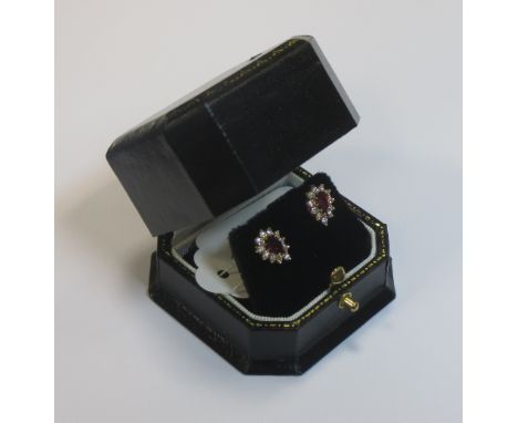 A pair of ruby and diamond earstuds, the pear shaped rubies surrounded by small round brillinat cut diamonds, all claw set in