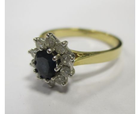 An 18ct sapphire and diamond cluster ring, the deep blue oval cut sapphire surrounded by ten small round brilliant cut diamon