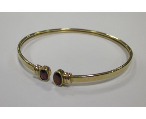 A yellow precious metal open ended bangle, set to ends with faceted oval garnets, cased  
