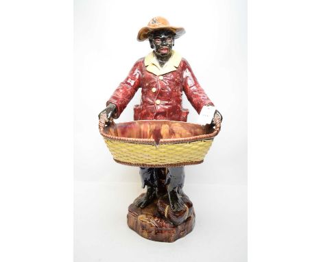 A ceramic Majolica figure of a man, modelled standing holding a wide wickerwork effect basket, 67cms high.
