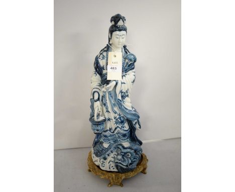 A Chinese blue and white ceramic figure of Guanyin, raised on a naturalistic wooden base, 47cms high. 