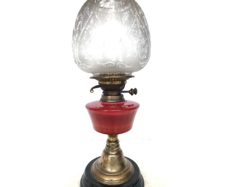 Victorian cranberry glass oil lamp with brass fittings and an etched glass shade. It features a pedestal base with a rich pat