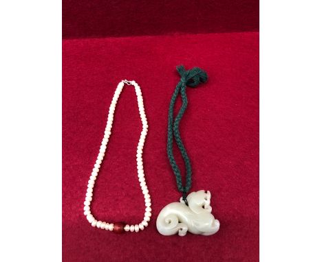 A CHINESE NEPHRITE JADE PENDANT PIERCED AND CARVED AS A QILIN.   W 6.5cms. TOGETHER WITH A STRING OF PEARL BEADS WITH A CORNE