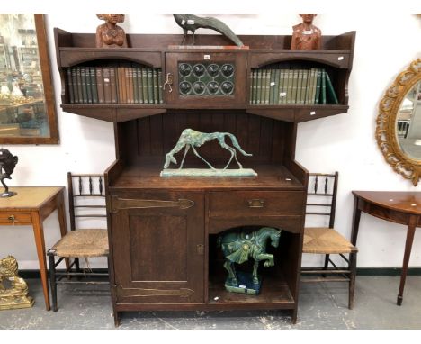 AN ARTS AND CRAFTS OAK SIDE CABINET BY LIBERTYS, THE BACK WITH THREE SHELVES ARRANGED ABOUT A LEADED BOTTLE GLASS DOOR, THE B