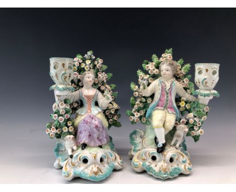 A PAIR OF PATCH MARK DERBY FIGURAL CANDLESTICKS, THE SHEPHERD AND SHEPHERDESS SEATED AMONGST FLOWERING BOCAGES.   H 17cms