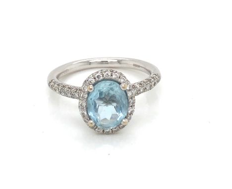 AN 18ct HALLMARKED GOLD BLUE TOPAZ AND DIAMOND RING. THE CENTRAL OVAL TOPAZ IN A RAISED FOUR CLAW SETTING WITHIN A HALO OF DI