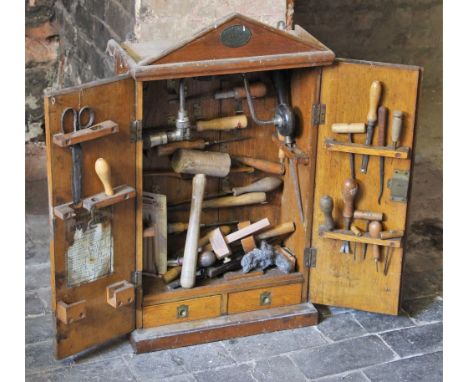 * An Army &amp; Navy wall mounted oak tool cabinet, early 20th century, of architectural form, the twin cupboard doors openin