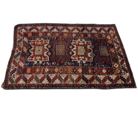 A Kazak wool rug, in red blue and brown colourways, the central field with alternating geometric medallions upon a blue groun