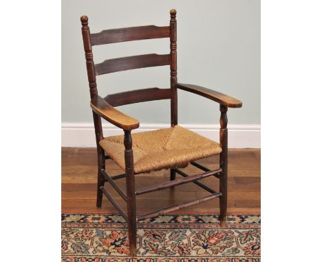 * A 19th century ladder back and rush seated elbow chair, the out swept arms upon turned supports enclosing the envelope rush