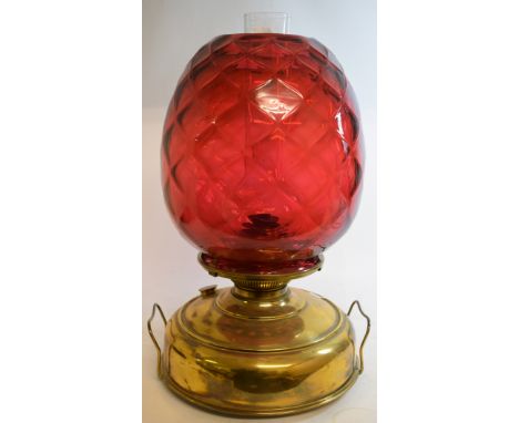 A large oil lamp, with a quilted cranberry glass shade on a brass reservoir, 45 cm high 