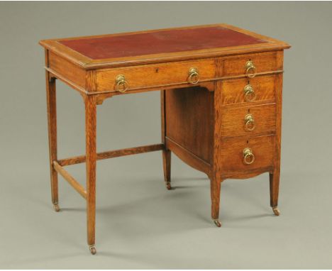 An Edwardian oak desk, with red leather writing surface, moulded edge and fitted with a series of drawers, raised on tapered 