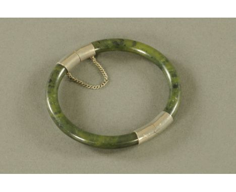 A Chinese jade bangle with silver coloured metal mounts, external diameter 8 cm, internal 6.5 cm.