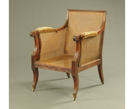 A Regency mahogany library bergere armchair, with loose cushions, padded arms and raised on sabre front legs.  Height to top 