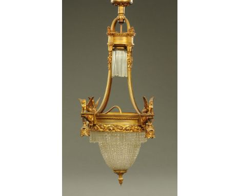 An antique gilt metal ceiling light fitting, of bag form with faceted glass drops and with winged sphinx decoration.  Height 
