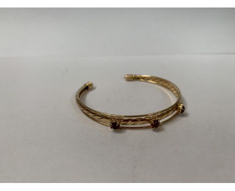 A YELLOW METAL BANGLE WITH RED STONE DESIGN 