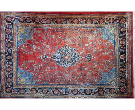 A large Kashan style rug, with a central foliate medallion on a ruby ground with palmette and vine motifs within multiple cor