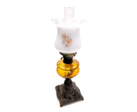 An early 20thC oil lamp, with an opaque shade, decorated with flowers, an amber glass central reservoir, on a cast iron base,