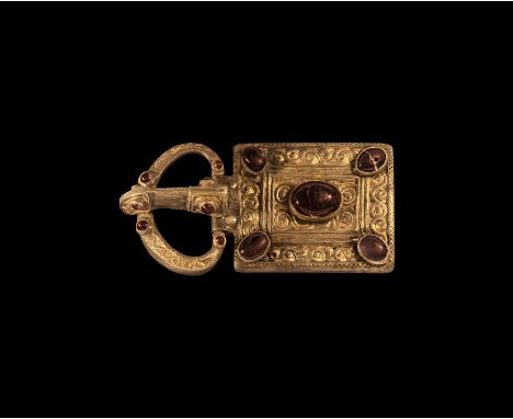 6th century AD. A silver-gilt buckle set comprising: broad loop with scroll detailing to the upper face, four inset garnet ca