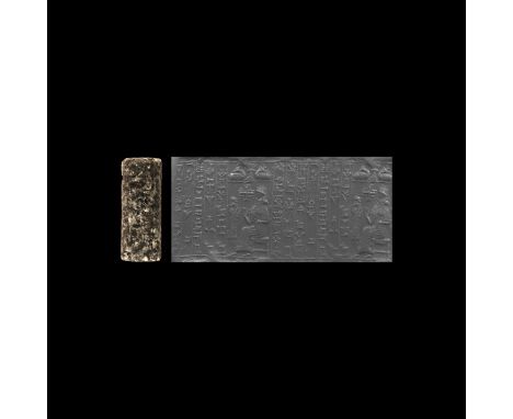 1500-1155 BC. A substantial granite cylinder seal with bearded king in a long robe, both hands raised to prayer, stands facin