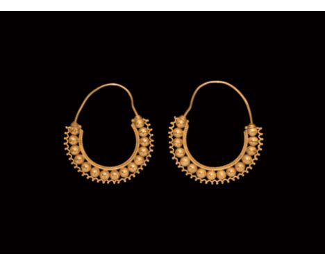 4th-7th century AD. A matched pair of gold earrings, each a wire hoop and band of hollow spheres with filigree cordon to the 