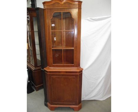 A light wood (yew) corner cabinet.