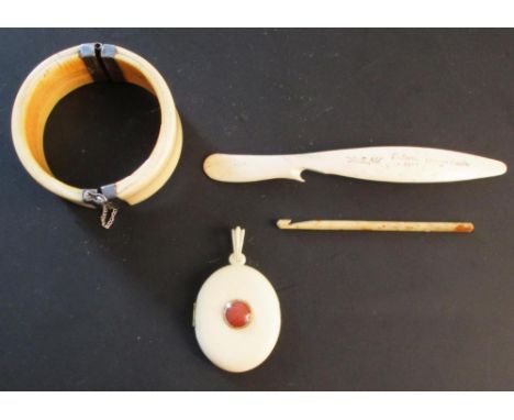 An ivory bangle, a locket, an 'Orange Peeler' and a crochet hook, the bangle with white metal hinges and clasp, the locket go