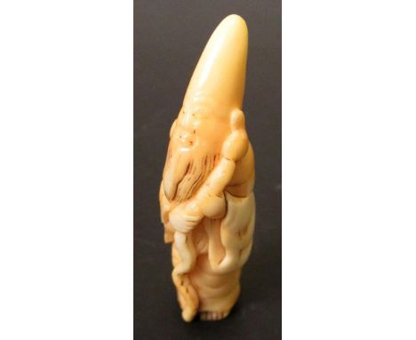 A 19th century tooth netsuke carved as Fukurokuju, the tall headed deity stand holding his rustic staff, 5cm (2 in) high  