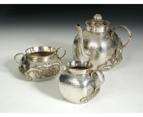 An early 20th century silver three piece tea service, each rounded square body hammered, bamboo handles growing from a rocky 