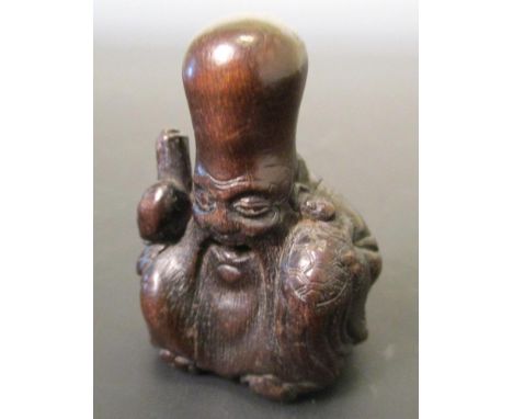 A 19th century wood netsuke carved as Fukurokuju seated laughing holding a scroll in his right hand and with a minogame climb