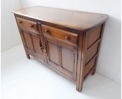 An Ercol-style elm dresser base; the overhanging top above two half-width drawers and two panelled cupboard doors below enclo