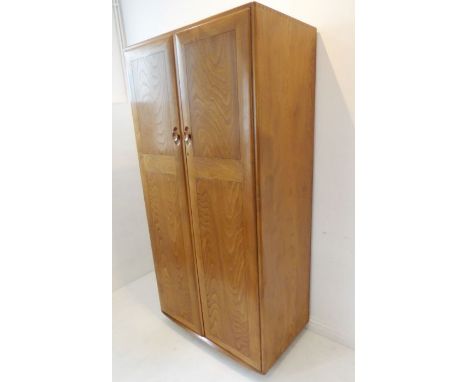 A fine quality Ercol-style elm wardrobe; two panelled doors opening to reveal hanging space, raised on castors (91cm wide x 5