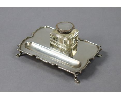 A George V silver desk inkstand with shaped border, pen-trough to one side, fitted square glass inkwell with hinged silver li