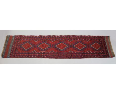 A Meshwani runner of madder ground, with row of five central lozenges within multiple geometric borders; 8’10” x 2’.