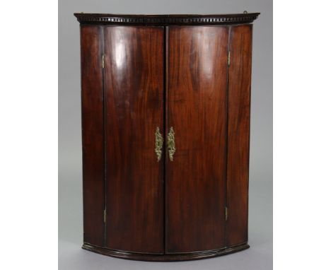 An 18th mahogany bow-front hanging corner cupboard with moulded dentil cornice above three shelves enclosed by pair of panel 