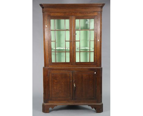 A late 18th century oak tall standing corner cupboard fitted two shaped shelves enclosed by pair of glazed doors above a pair