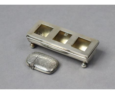 An Edwardian silver three-division postage stamp box, the trough-shaped base on four ball feet, the spring-loaded flat hinged