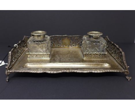 A 19th century silver desk stand, with pen rest and two cut glass inkwells, having pierced sides, raised on scrolling feet, T