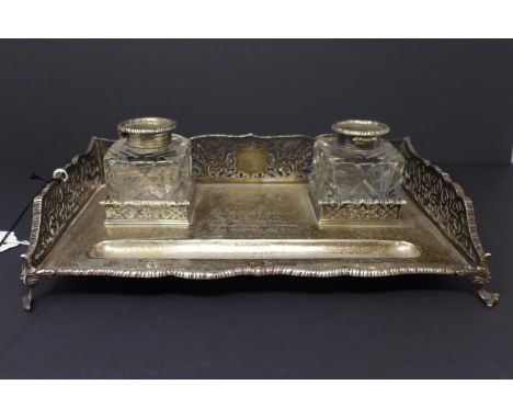 A 19th century silver desk stand, with pen rest and two cut glass inkwells, having pierced sides, raised on scrolling feet, T