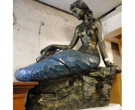 A modern fibreglass and lead light lamp in the form of a mermaid on a rock.