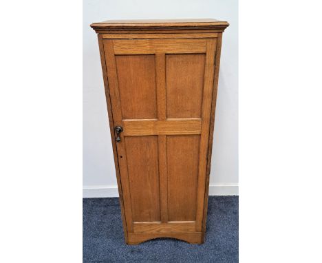 1930s NARROW OAK CABINETwith a moulded top above a panelled door opening to reveal a shelved interior with a slatted back pan