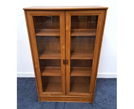 TEAK EFFECT BOOKCASE with a rectangular top above two glass panel doors opening to reveal a shelved interior, standing on a p