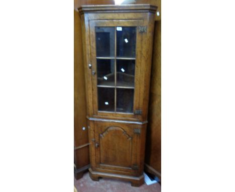 A 65cm reproduction antiqued oak corner cabinet with glazed panel door to top, canted sides and panelled door under, set on b