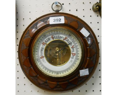 A 22cm diameter early 20th Century carved walnut framed aneroid wall barometer with petal border and visible works