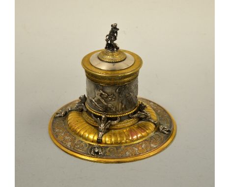 A CAST WHITE METAL INKWELL, with relief moulded classical scenes and figures over gilt reeded step to circular gilt scroll in