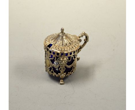 A WHITE METAL MUSTARD, with pierced decoration, lion mask mounts, urn finial, on three paw feet with blue glass liner, approx