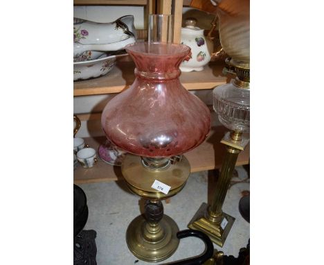 OIL LAMP WITH UNUSUAL GRENADE FORMED BASE, BRASS FONT AND A CRANBERRY TINTED SHADE